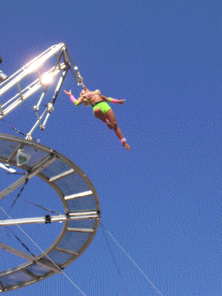 Tina hangs in mid air by nothing but a thin strap as she circles the disk.