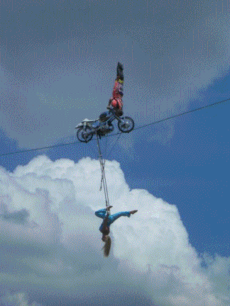 John performs a handstand on his motorcycle high in the air on the Sky Cycle while Tina hangs upsidedown